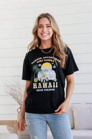 A woman smiling and wearing a black short-sleeved crew neck t-shirt with 'HAWAII' and 'Black Paradise' printed on the front, paired with blue jeans.