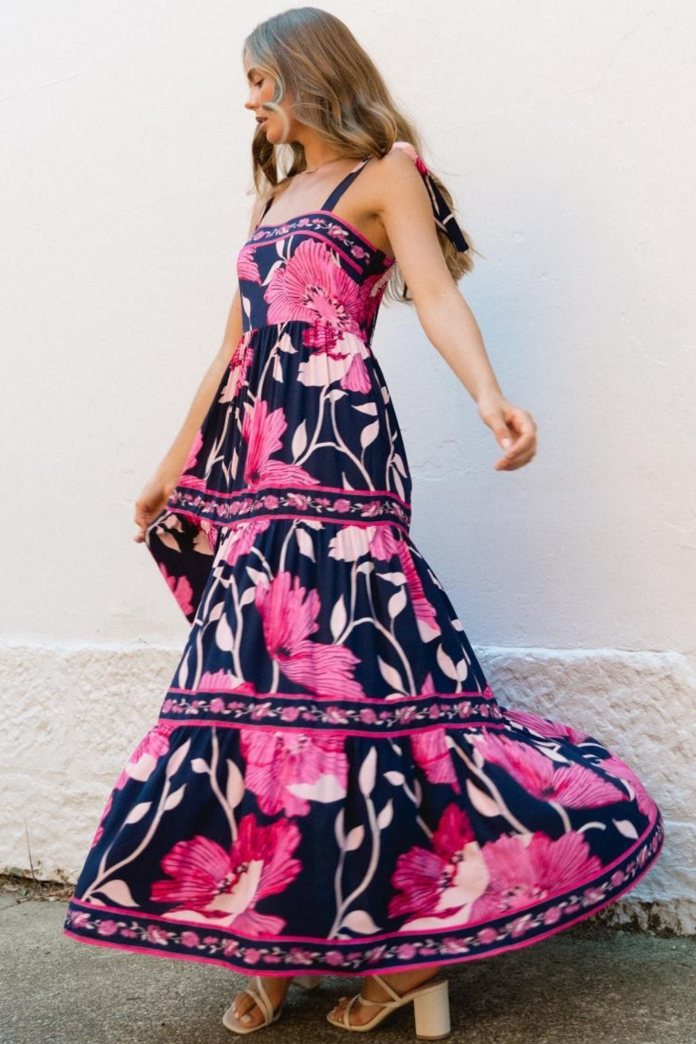 Woman wearing a floral dress with pink and purple flowers against a white wall.