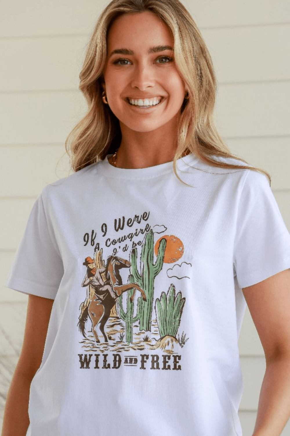 Woman modelling a white cotton graphic t shirt with a cowgirl in a desert graphic and slogan 'If i were a cowgirl i'd be wild and free'.