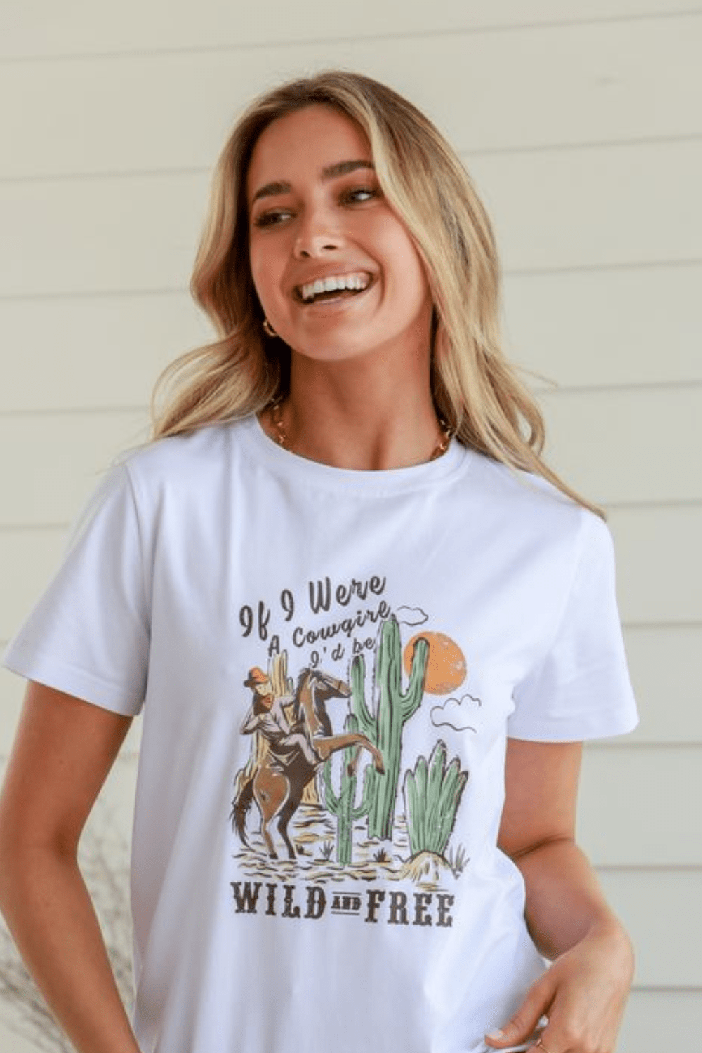 Woman modelling a white cotton graphic t shirt with a cowgirl in a desert graphic and slogan 'If i were a cowgirl i'd be wild and free'.