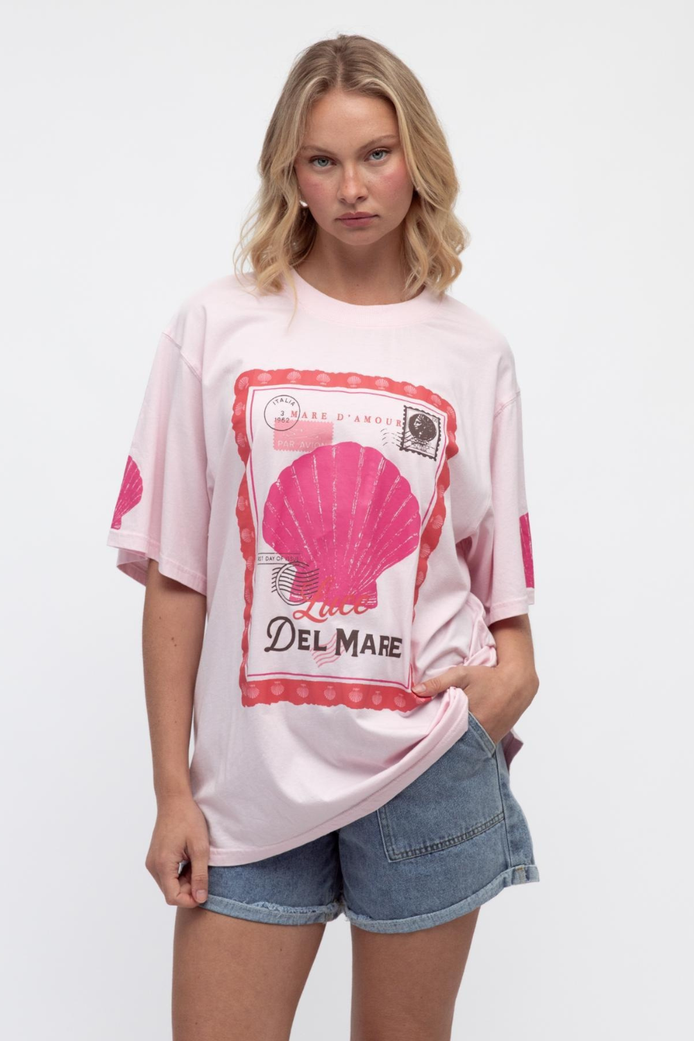 Woman wearing a pink t-shirt with a shell graphic and 'Del Mare' text on a white background