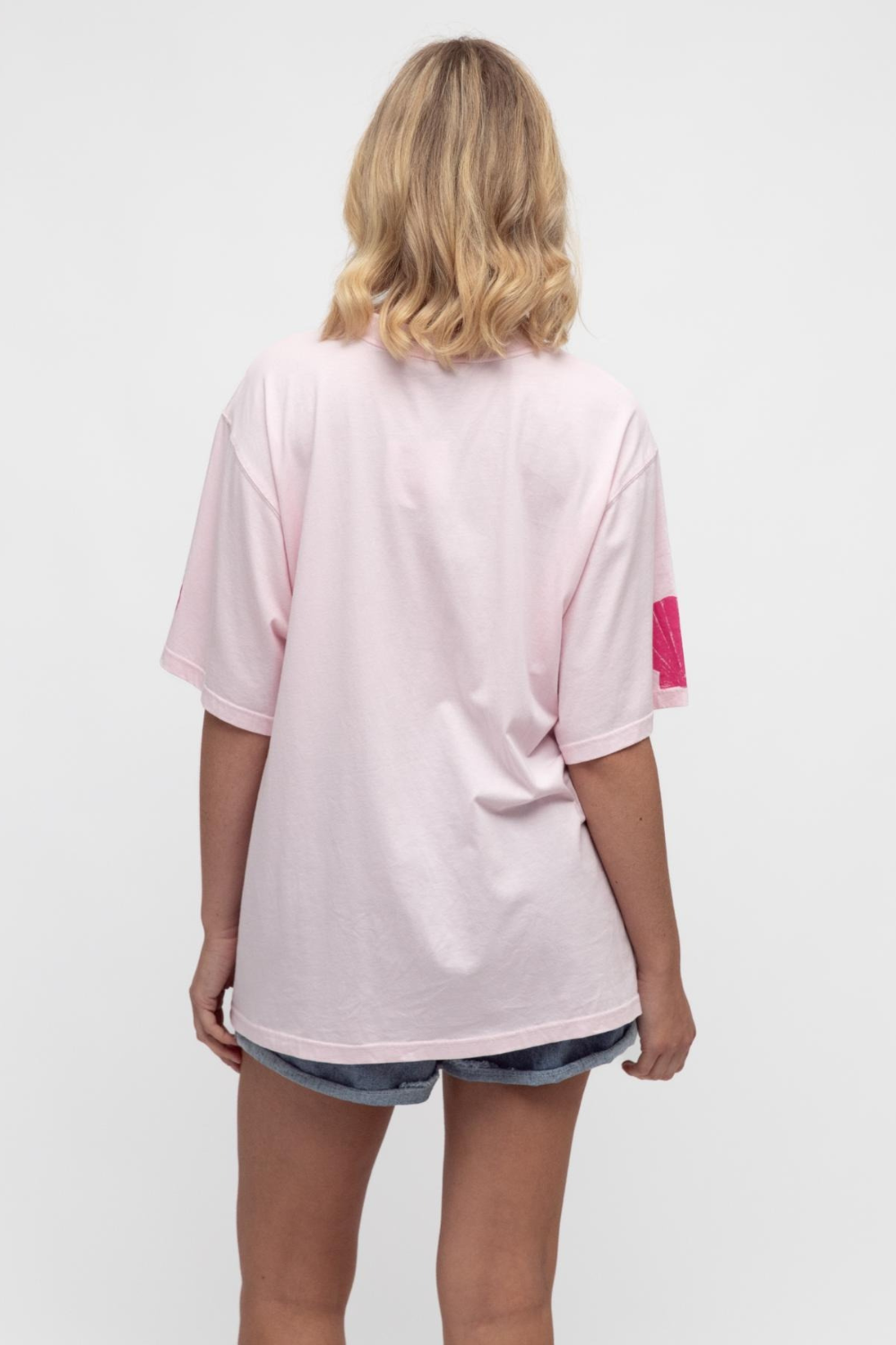 Person wearing a light pink t-shirt with a small red logo on the sleeve against a white background