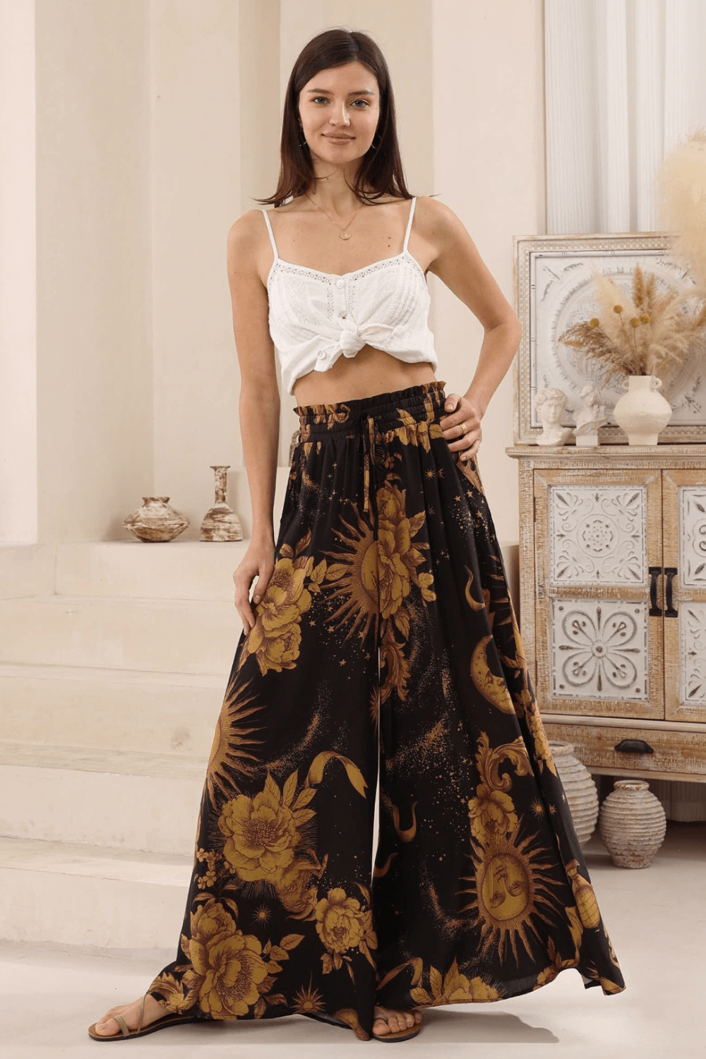 A model wearing high-waisted, boho style, wide-leg pants with a celestial print in a night sky color palette.
