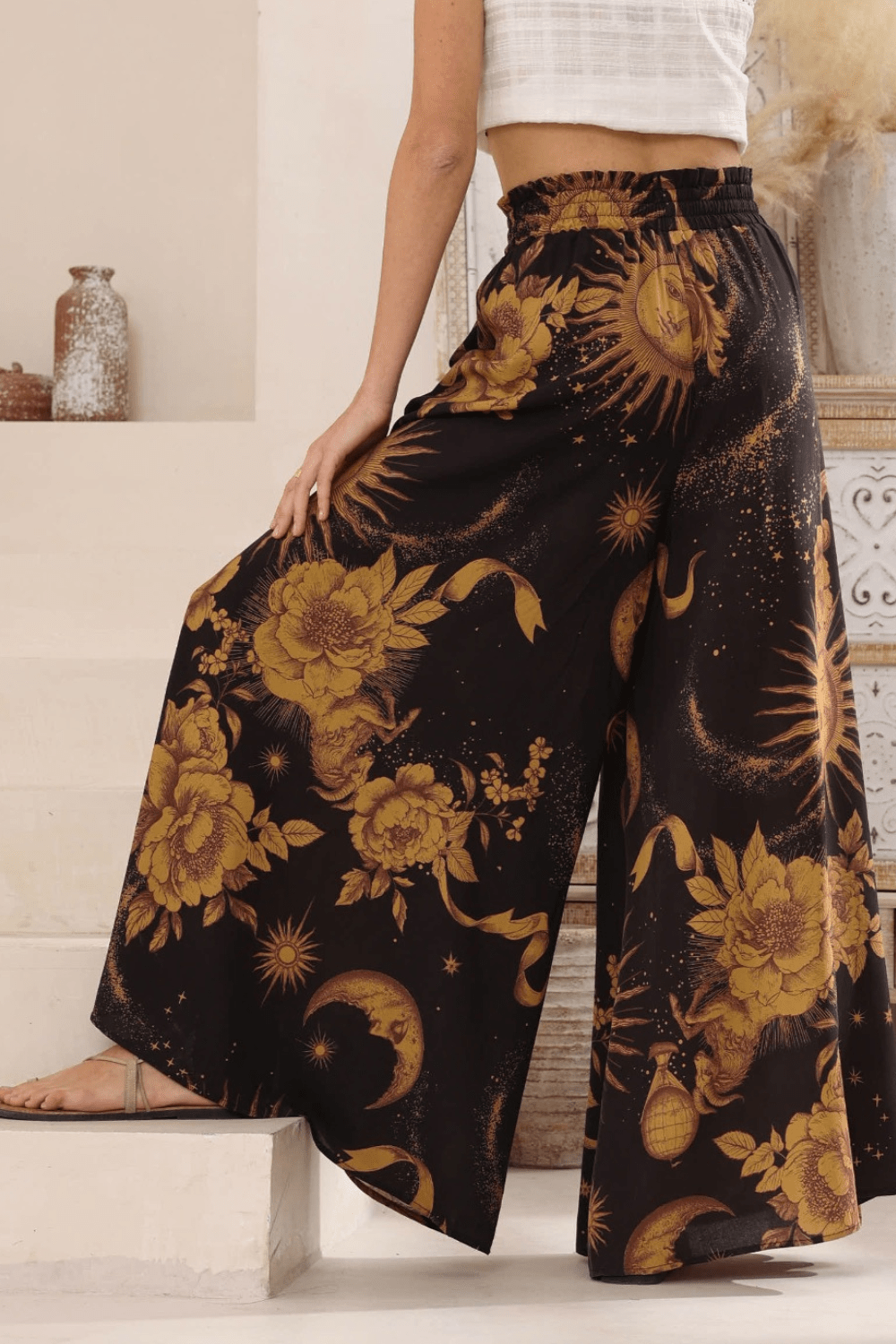 A model wearing high-waisted, boho style, wide-leg pants with a celestial print in a night sky color palette.