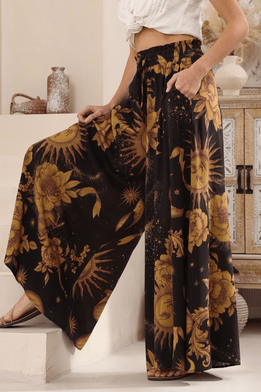 A model wearing high-waisted, boho style, wide-leg pants with a celestial print in a night sky color palette.