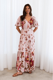 A woman wearing a floral maxi dress with a flattering v-neckline, short balloon sleeves with elastic cuffs, and an adjustable drawstring waist with side ties.