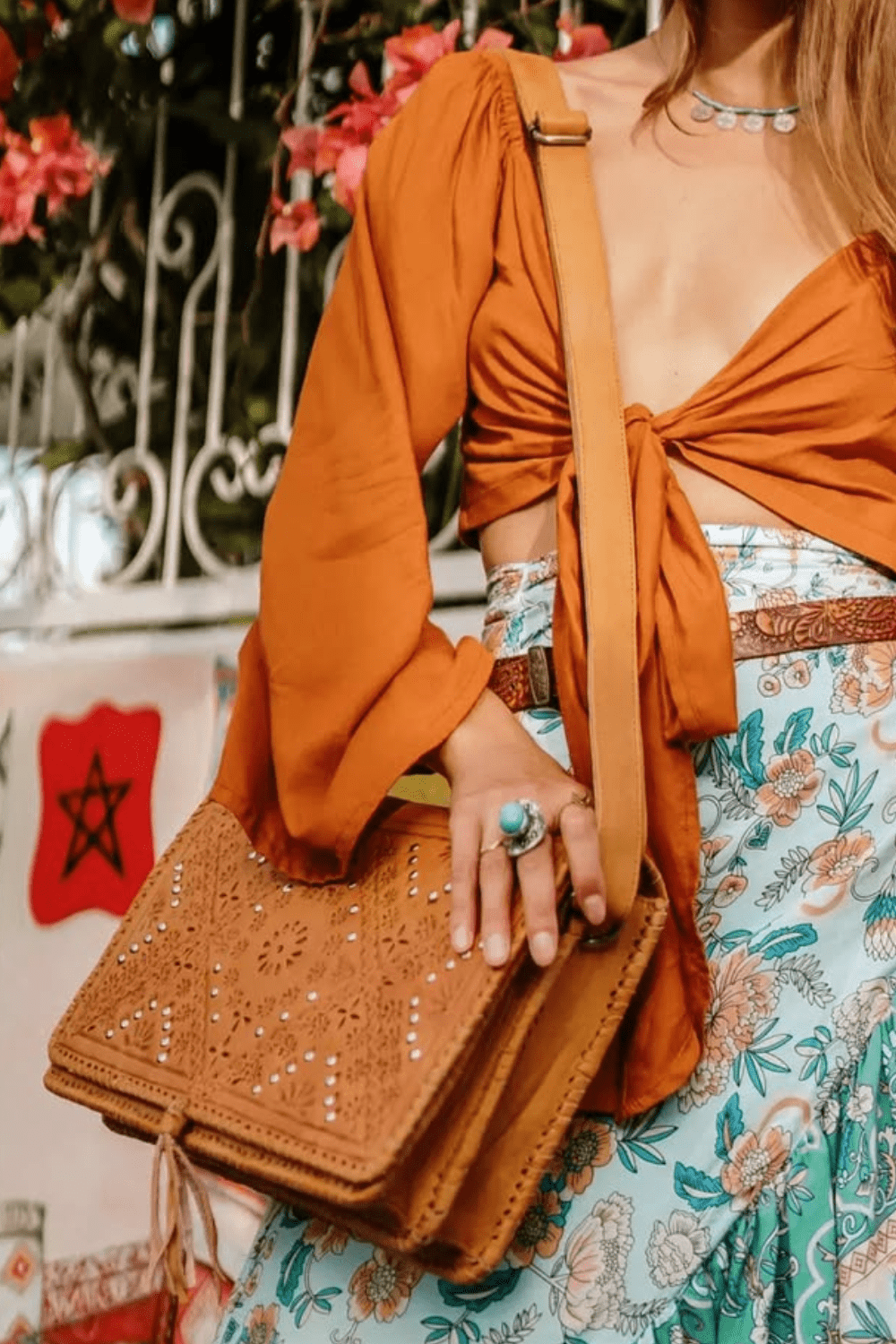 A person holding a tan leather satchel handbag with intricate hand-tooled details and stud embellishments.