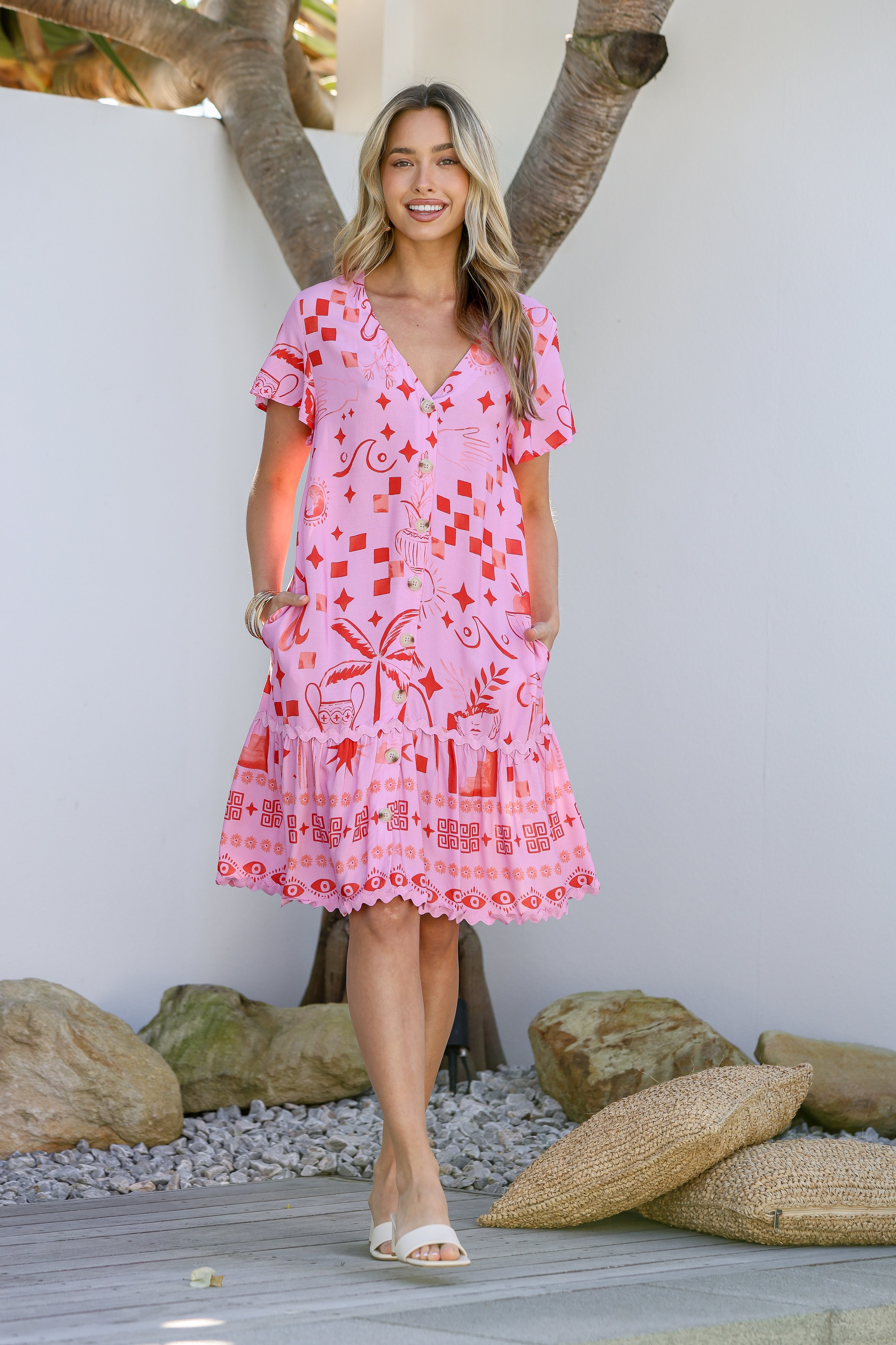 A woman wearing a pink mini dress with a tropical-inspired print and ric rac trim, featuring a V-neckline and short sleeves.
