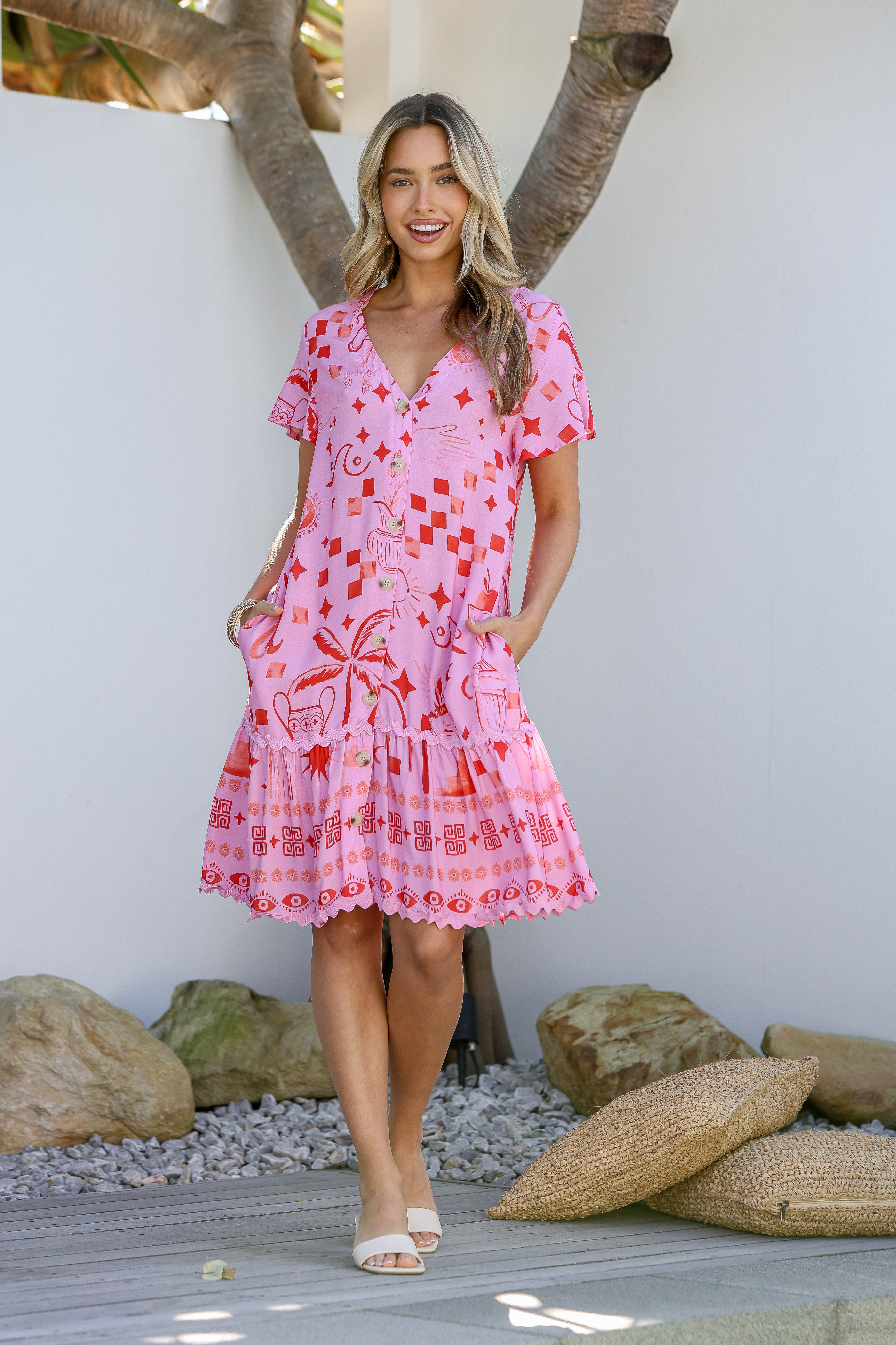 A woman wearing a pink mini dress with a tropical-inspired print and ric rac trim, featuring a V-neckline and short sleeves.