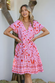 A woman wearing a pink mini dress with a tropical-inspired print and ric rac trim, featuring a V-neckline and short sleeves.