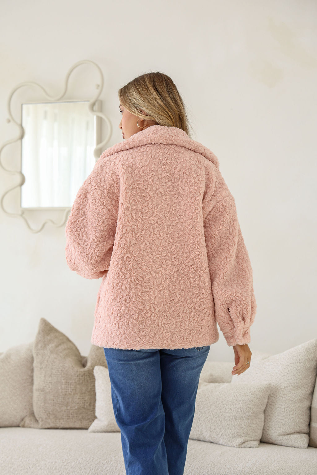 Person wearing a pink fluffy coat standing in a living room.