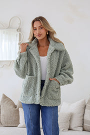 A woman wearing a sage green teddy boucle jacket with a wide collar, button-through front, and two front patch pockets.