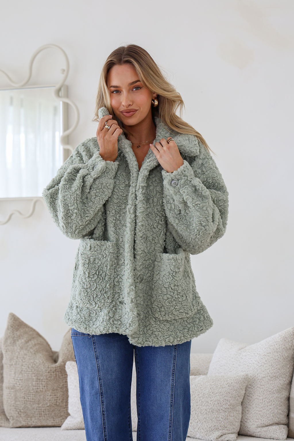 Woman wearing a green sherpa jacket in a cozy living room setting