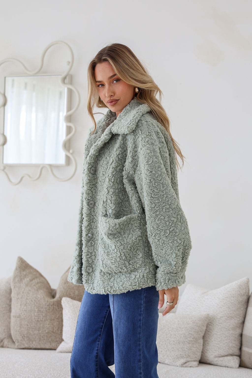 Woman wearing a green sherpa jacket in a cozy living room setting.