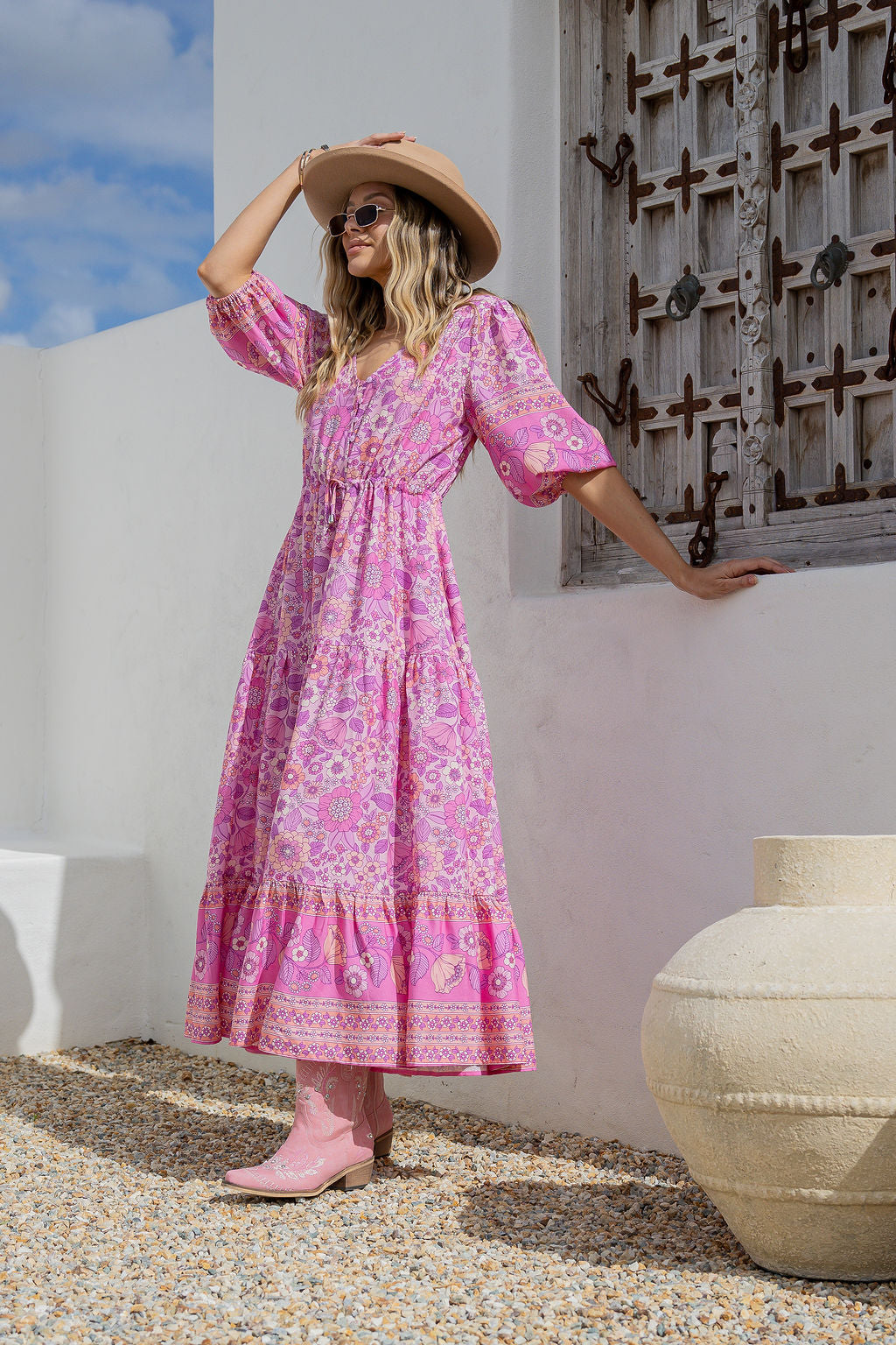 Woman in a pink dress standing against a white wall with a decorative door.