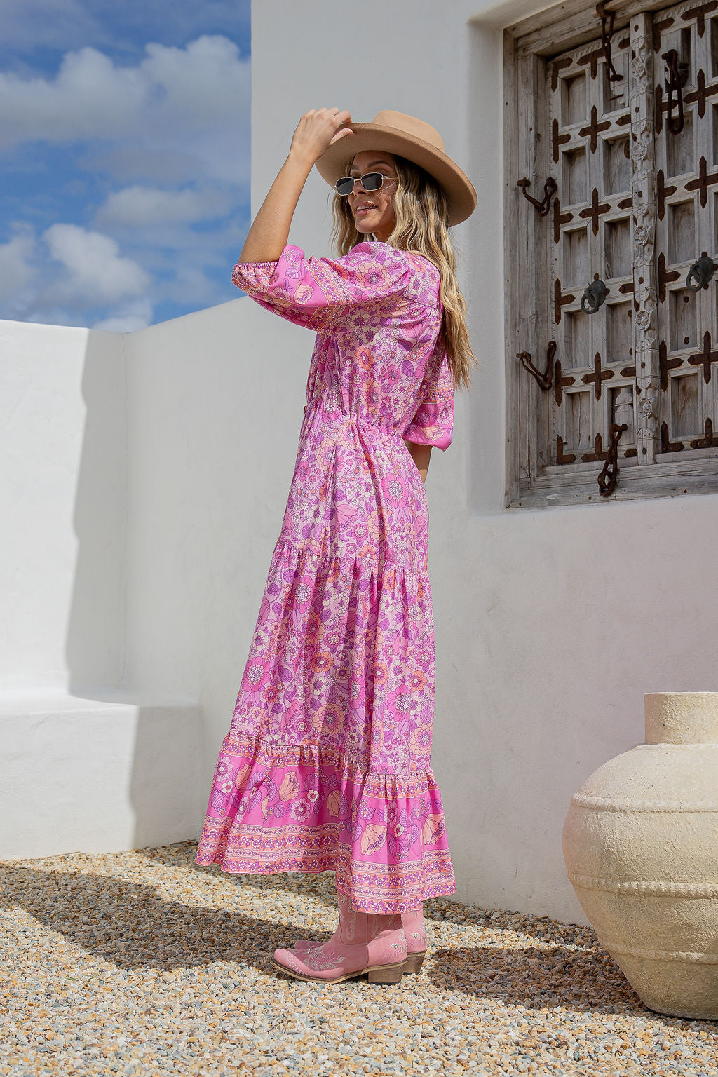 Woman in a pink dress standing in front of a white wall with a decorative wooden door.