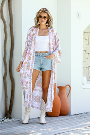 A woman standing outdoors wearing a floral kimono with boho-inspired border, paired with a white tank top and blue shorts.