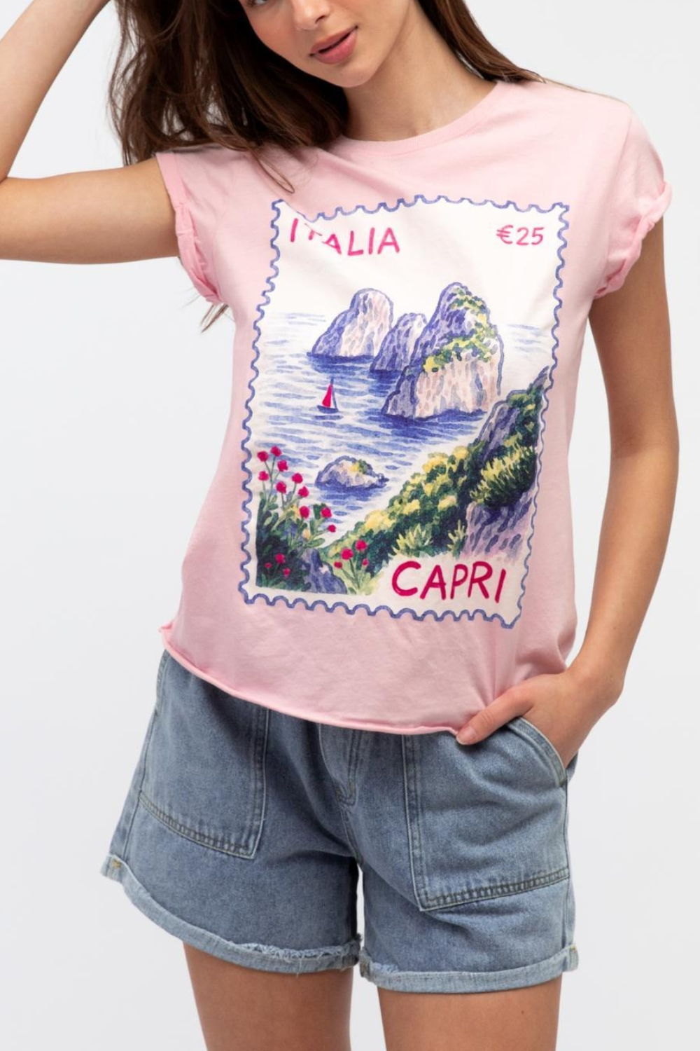 Person wearing a pink t-shirt with Capri stamp design and denim shorts on a white background