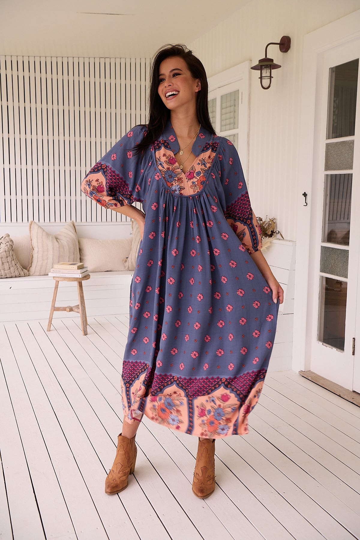 A woman standing in an indoor setting wearing a bohemian style midi dress with long sleeves, in a floral and geometric pattern, with an open neckline.