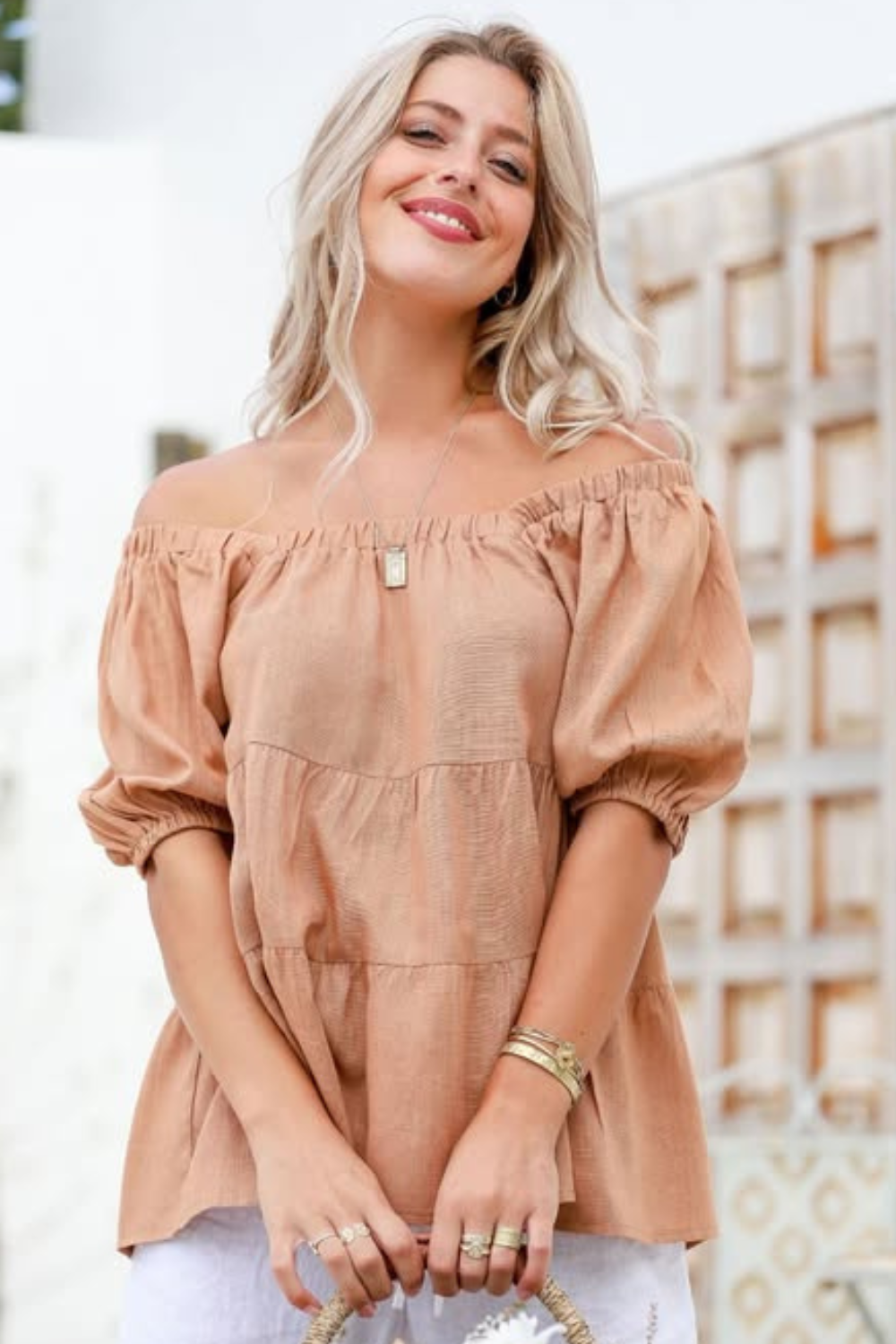 A woman wearing a brown linen tiered top with a square neckline and puff sleeves, paired with white pants.