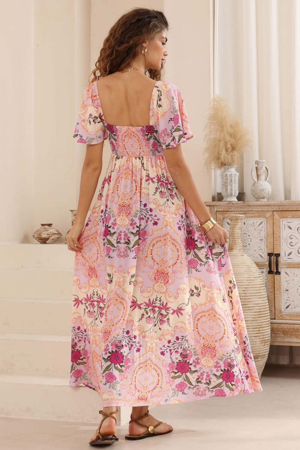 Woman wearing a floral dress in a room with a wooden cabinet and decorative items.