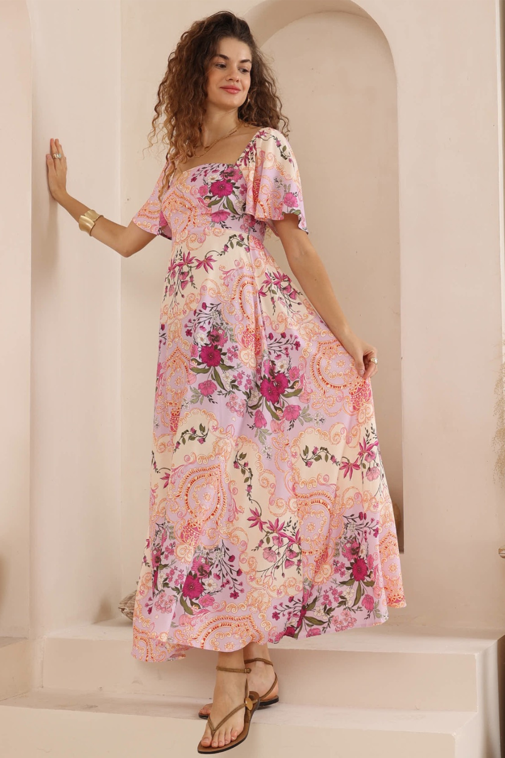 Woman wearing a floral dress standing against a neutral wall.