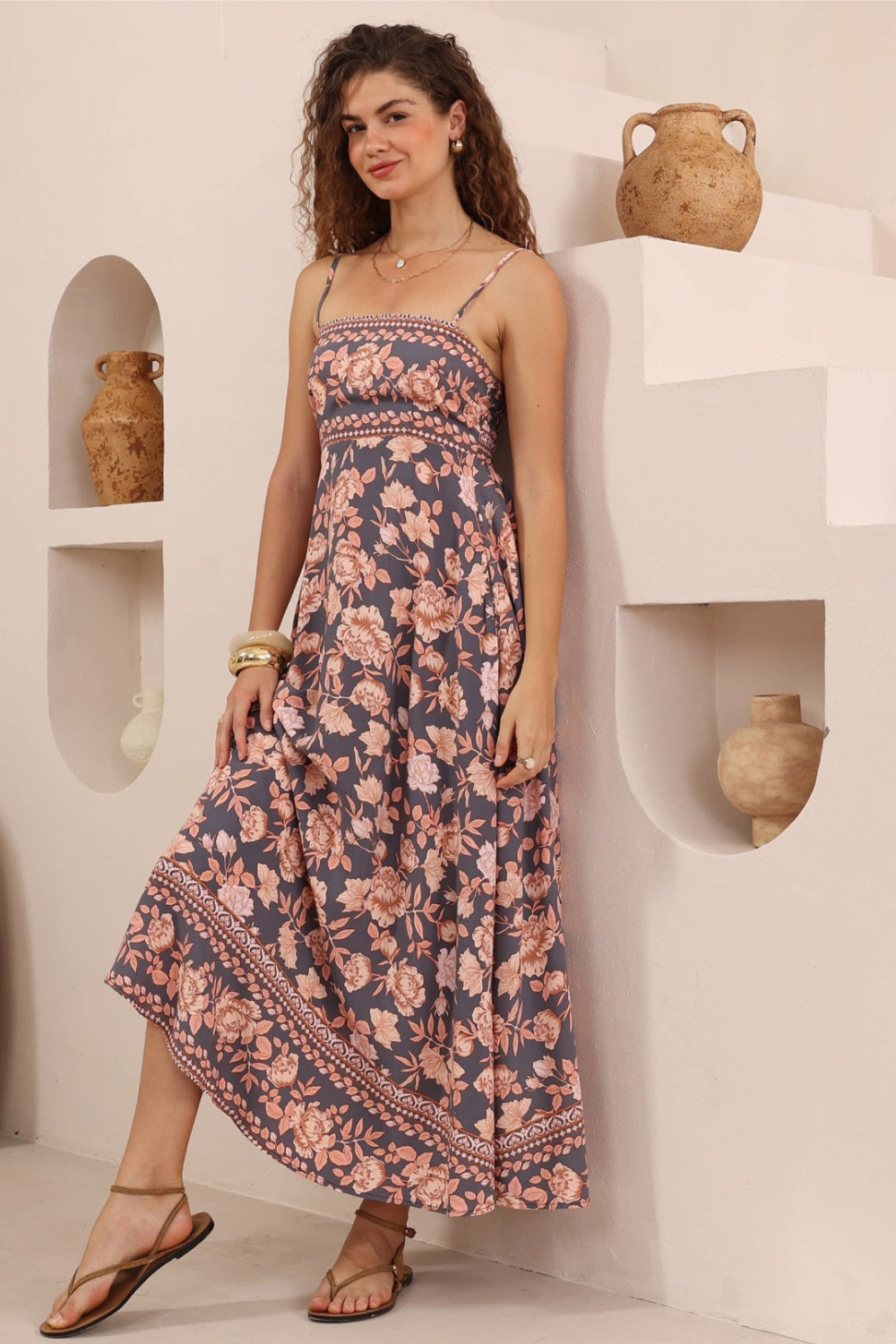 Woman wearing a floral dress standing in a room with white walls and decorative vases.