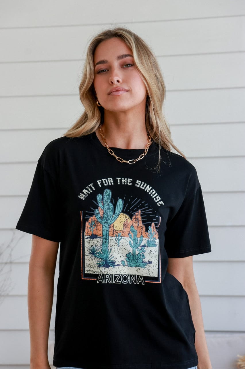 Woman smiling modelling a black cotton graphic tee with Cacti in the desert and the slogan 'Wait for the sunshine, Arizona'
